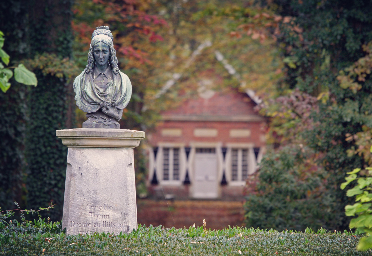 B&uuml;ste, die das Abbild von Annette von Droste-H&uuml;lshoff zeigt. Die B&uuml;ste steht auch einem Sockel im Park von Burg H&uuml;lshoff. Im Hintergrund liegt das &raquo;Teeh&auml;uschen&laquo;. Der Blick von Droste ist nach unten gerichtet. Ihre Haare sind, f&uuml;r die Zeit des Biedermeier typisch, am Hinterkopf hochgesteckt und an den Schl&auml;fen gelockt.